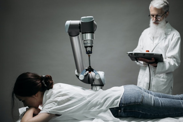 Robotic arm treating a patient lying on a table while a doctor controls it from a tablet