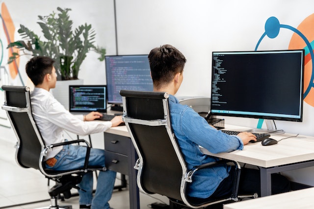 Two developers at their desks writing code on large monitors in an office