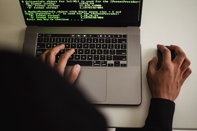 Hands typing on a laptop showing green console output, one hand on a mouse