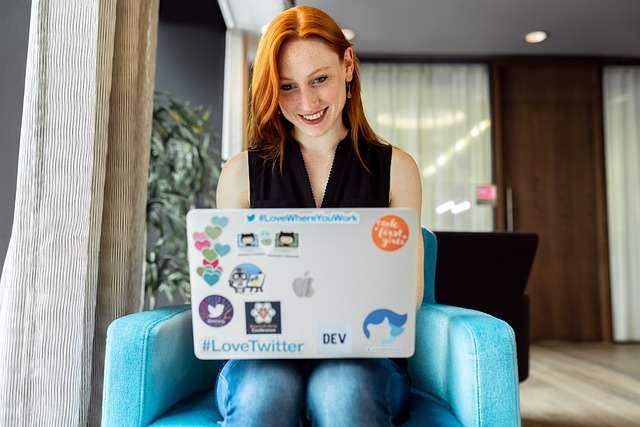 Smiling woman working on a sticker-covered laptop in a lounge chair