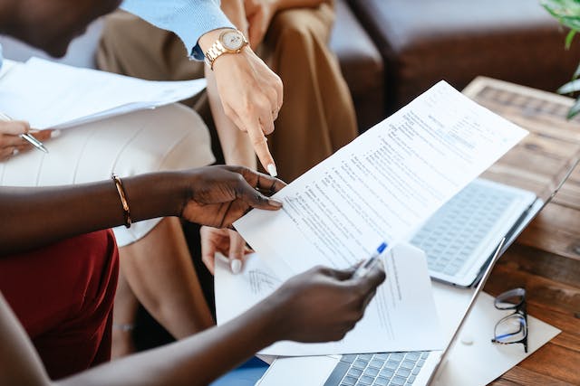 Colleagues reviewing printed documents together, one pointing at the page, with laptops nearby