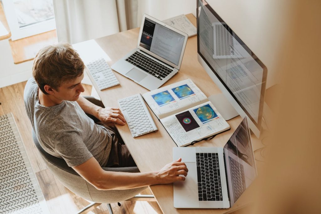 Overhead view of a developer at a desk with several laptops, a monitor and printed charts