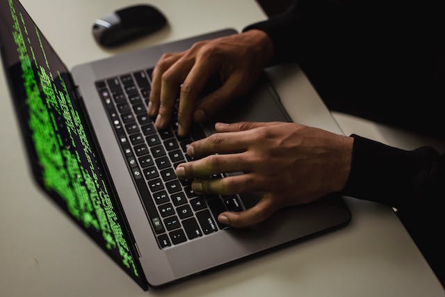 Close-up of hands typing on a laptop with green code on a dark screen