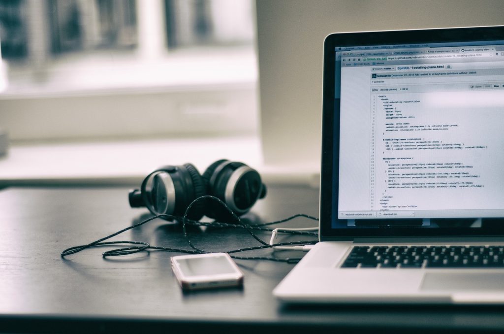 Laptop showing HTML and CSS code beside headphones and a smartphone on a desk