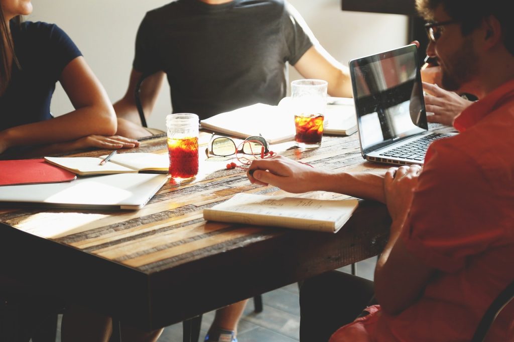 Small team meeting around a wooden table with laptops, notebooks and drinks