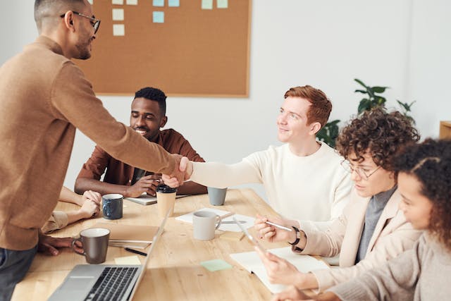 Man shaking hands with a colleague across a meeting table as the team looks on
