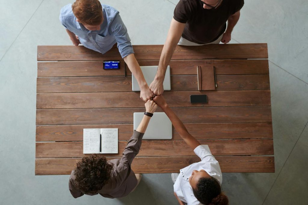 Overhead view of four colleagues bumping fists over a table with laptops