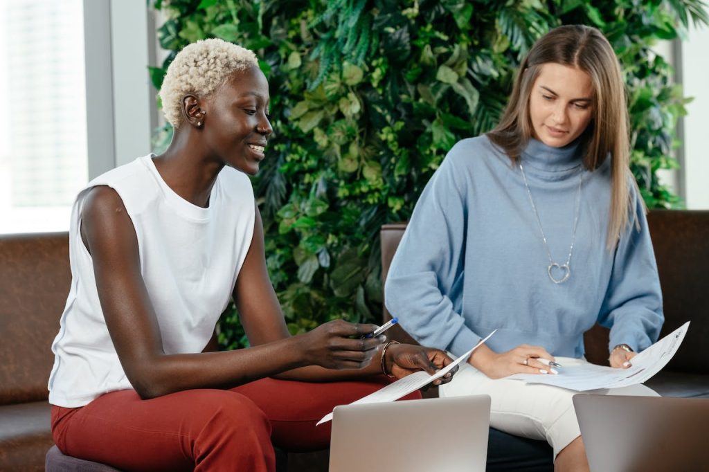 Two colleagues reviewing printed documents with laptops open in front of them