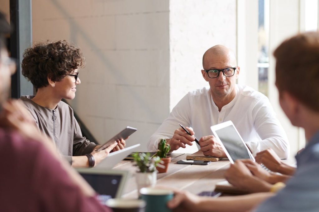 Colleagues in a meeting around a table using tablets and laptops
