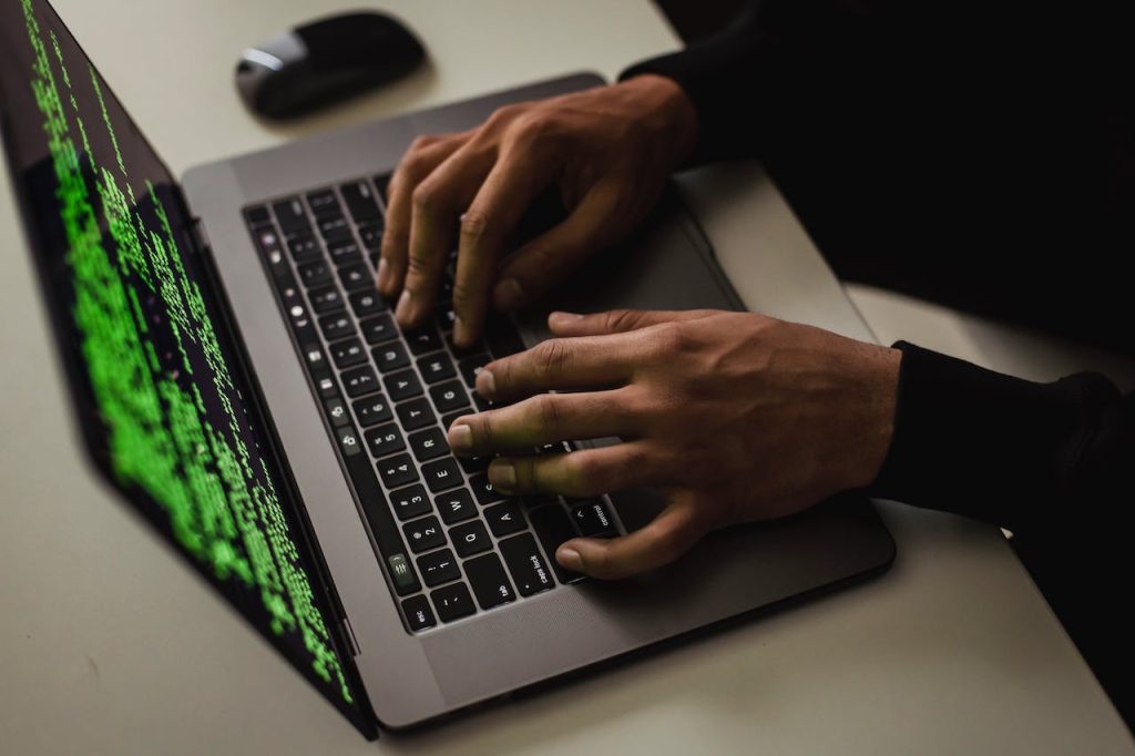 Hands typing on a laptop with lines of green code on the screen