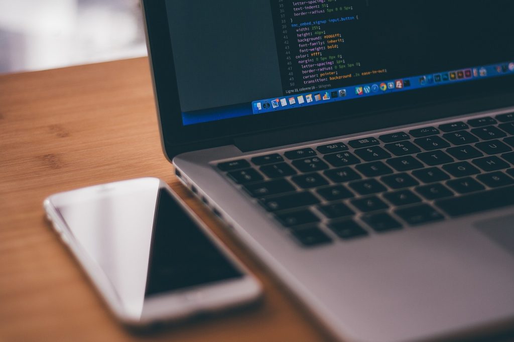 Laptop with CSS code on screen beside a smartphone on a wooden desk
