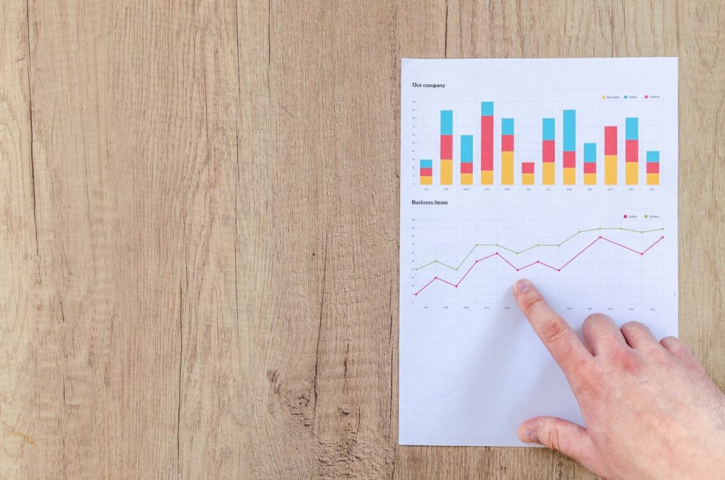 Finger pointing at printed bar and line charts on a wooden table