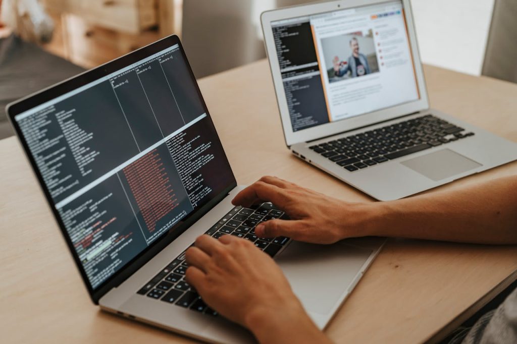 Hands typing on a laptop with terminal windows open, a second laptop beside it