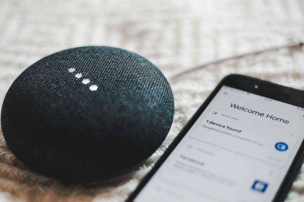 Smart speaker next to a smartphone showing a "Welcome Home" device setup screen