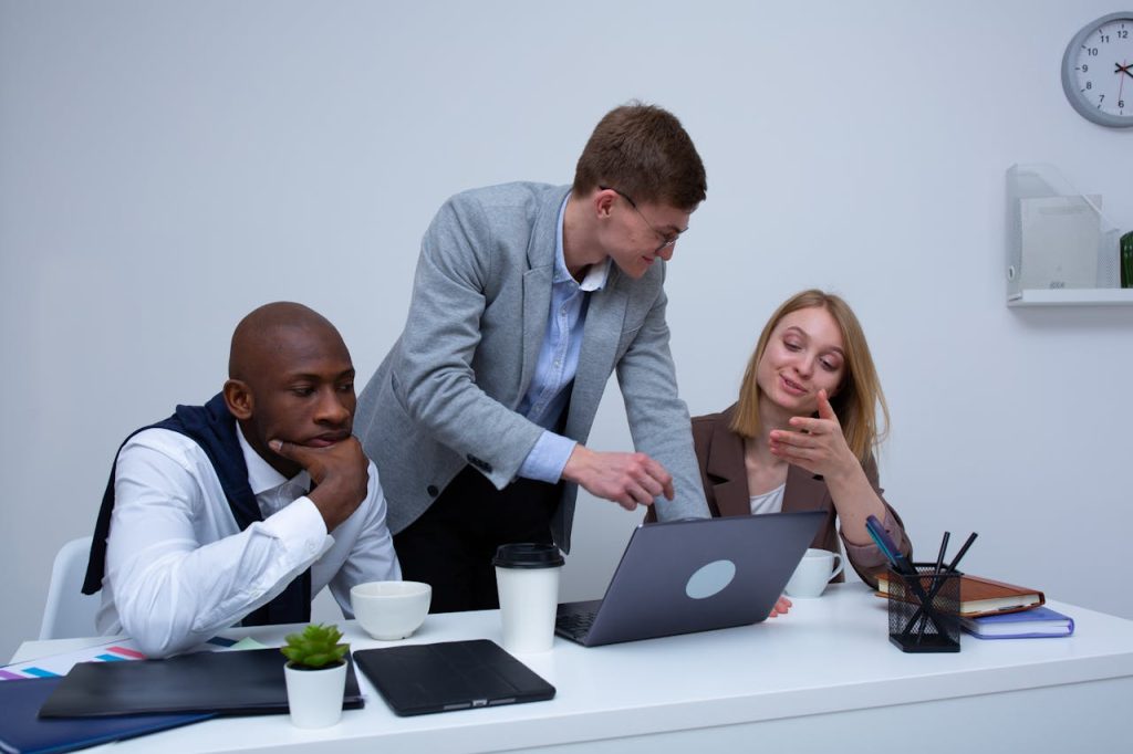 Colleague pointing at a laptop screen while explaining something to two seated coworkers