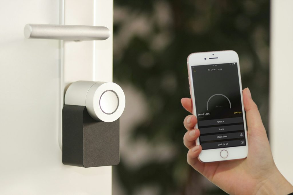 Hand holding a smartphone app that controls a smart lock on a door