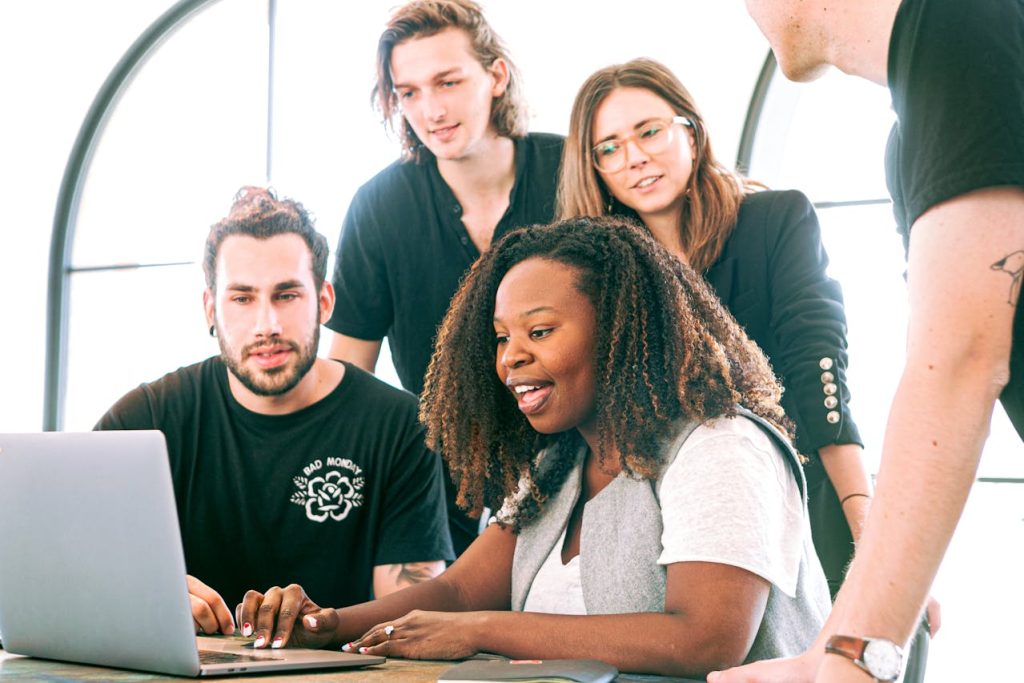 Group of colleagues gathered around a laptop, smiling at the screen