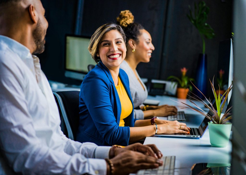 Smiling colleagues working side by side on laptops at a shared office desk