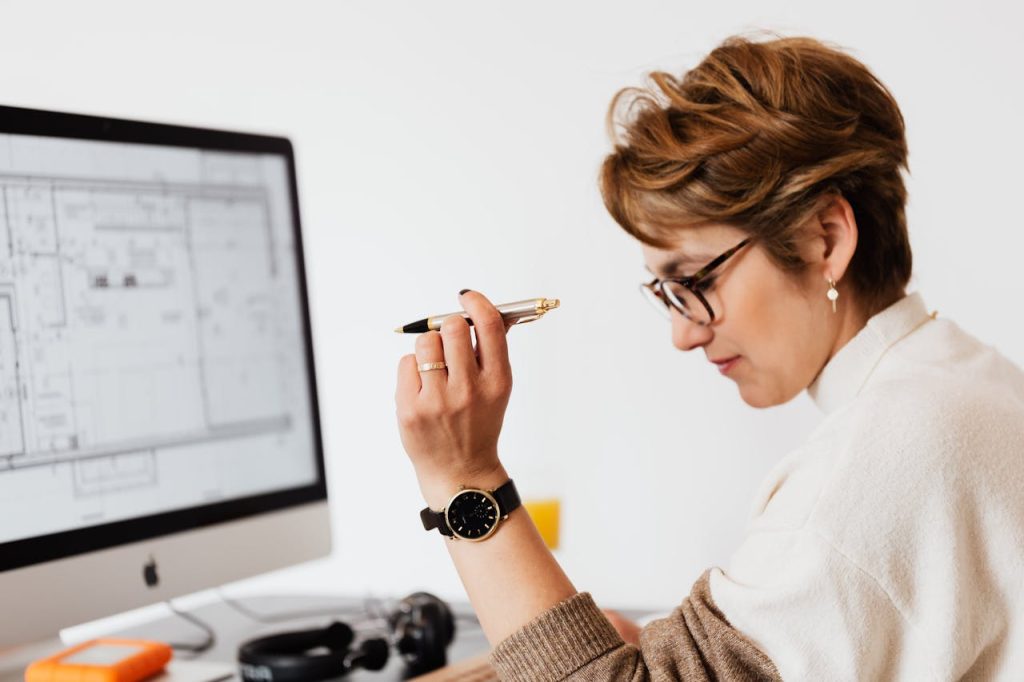 Woman holding a pen while reviewing an architectural floor plan on a desktop monitor