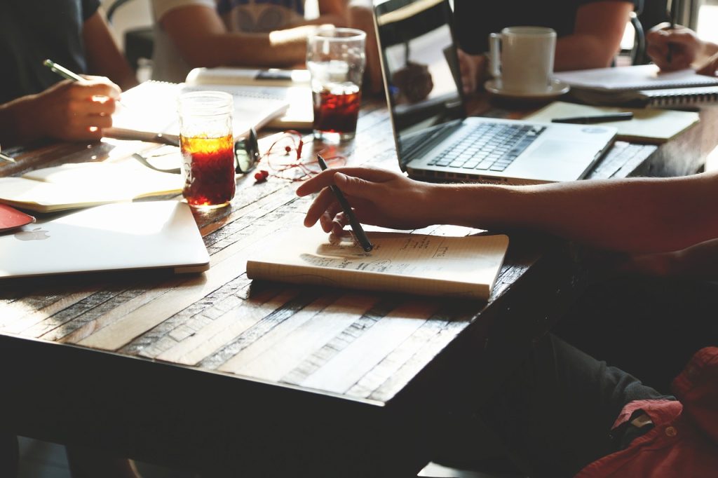 Team working around a wooden table with laptops, notebooks and drinks